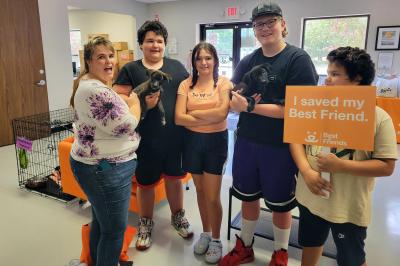 Family holding their two new puppies Grumpy and Sneezy and a sign that says 'I saved my best friend'