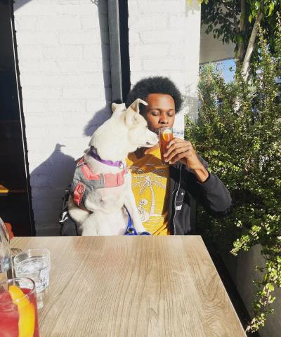 Person sipping a beverage at an outdoor restaurant while Elle the dog looks over