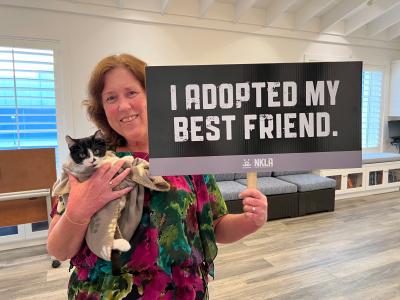 Person holding Ellie Williams the cat, along with a sign that says, 'I adopted my best friend'