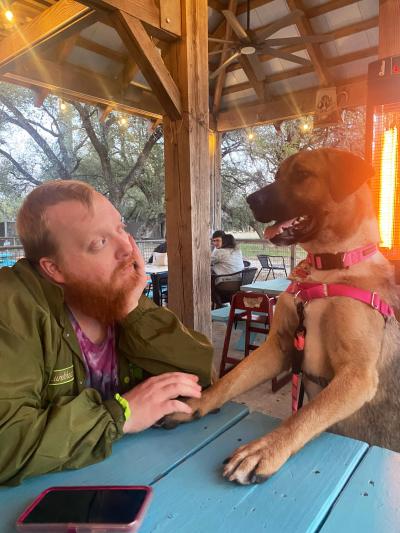 Person with chin in hand looking at Maya the dog in some covered outside seating