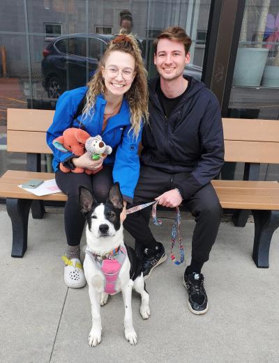 Two people sitting on a bench with Bunny the dog on a leash in front of them