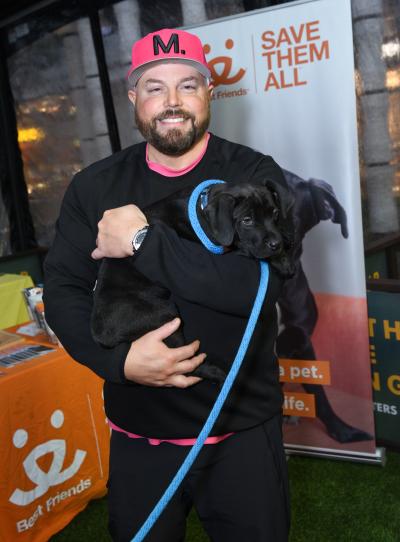 Mikael Lindnord, author of 'Arthur - The Dog Who Crossed the Jungle to Find a Home' holding a black puppy in front of a Best Friends banner