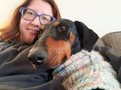 Selfie of Svea snuggling with Kizzy the dog, who is wearing a sweater