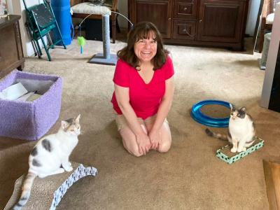 Marie in between Lola and Abby the cats, who are both sitting on cardboard scratchers