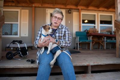 Laurie Shute holding RoiLie the dog in her lap with the dog's wheelchair beside them