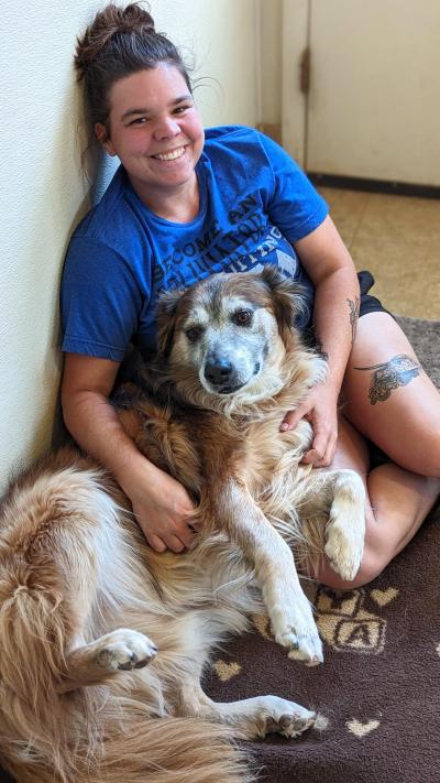 Mario the dog lying upside-down onto smiling person's lap, who is sitting on the ground