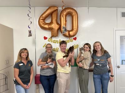 Volunteer Bill Coaker with cats and people beneath a large 40 balloon