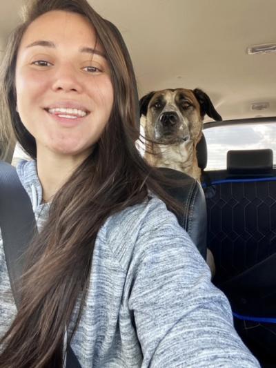 Ana in a vehicle front seat with Brutus the dog in the back seat