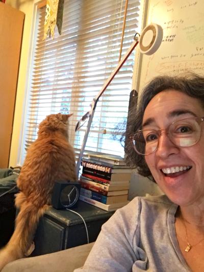 Selfie of Julie with Archie the cat sitting in the background looking out a window