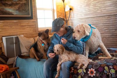 Kathy sitting on a bed with Edna, Astrid and Max the dogs