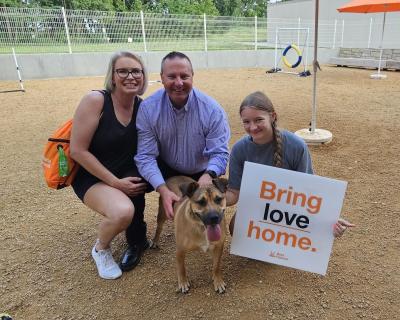 Doug the dog being adopted by his new family, who are holding a 'bring love home' sign