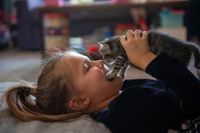 Child lying down and holding one of the dragon kittens to her face