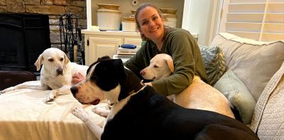 Smiling person sitting on a couch with three dogs