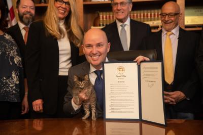 Utah Gov. Spencer Cox signing a document declaring 2024 No-Kill Shelter Year in Utah while holding a kitten with Best Friends representatives in the background