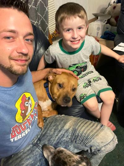 An adult and child sitting with a brown dog between them