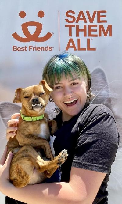 Athena holding Gremlin the dog in front of a Best Friends Save Them All logo