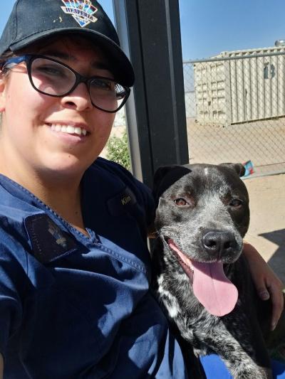 Smiling person sitting with arm around a smiling black and white dog