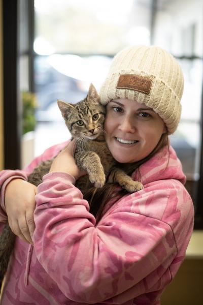 Person wearing a winter hat holding a tabby kitten