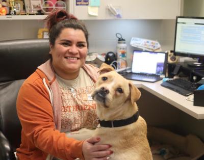 Smiling person wearing Best Friends branded clothing at a desk with a pit-bull-type dog