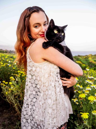 Smiling person holding Doja the cat in front of some flowers