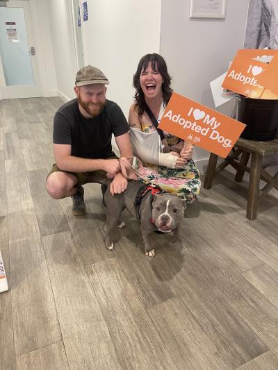 Two happy people with Rosie the dog, one person holding a sign that says, I heart my adopted dog