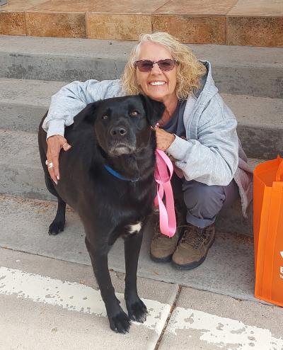 Jill smiling and sitting on some steps, hugging Finley the big black dog