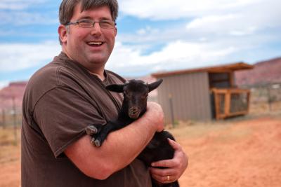 Emmett the lamb being held by a smiling person in front of a shed