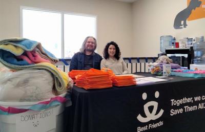 Two people sitting behind a table with Best Friends tablecloth, surrounded by donations for the kitten shower