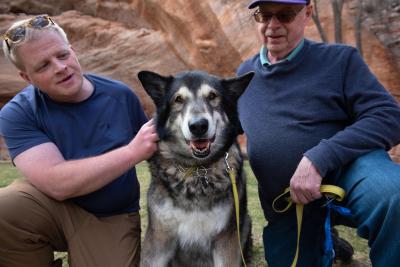 Shadow the dog between Ryan and another person with a red rock cliff behind them