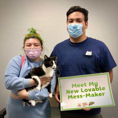 Two people wearing masks and holding a black and white cat and sign at the National Adoption Weekend