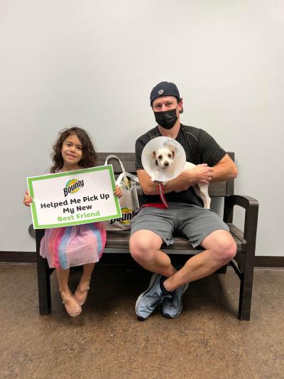 Two people sitting on a bench with a sign and a dog wearing a protective cone at the National Adoption Weekend