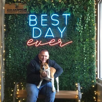 Wayne and Grover the dog on a bench below a sign that says, best day ever