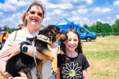 Black a tan puppy being held by an adult kissing the face of a kid at the Best Friends Super Adoption in Northwest Arkansas