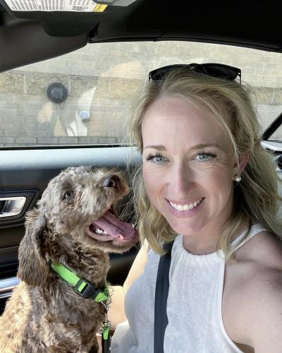 Bailey the dog in the side seat of a car with a smiling person