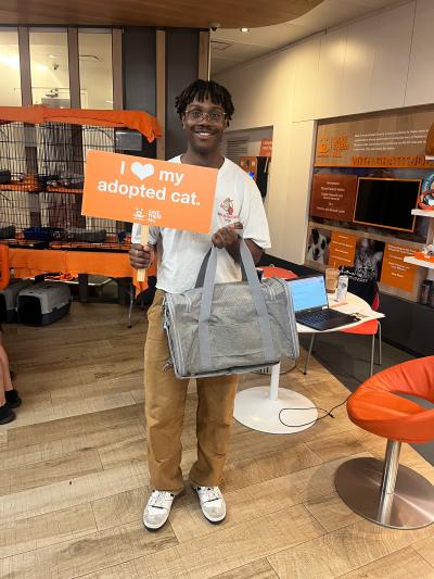 Smiling adopter holding a carrier containing his new cat and a sign that says, "I heart my adopted cat" at the Best Friends Lifesaving Center in New York City