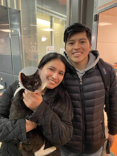 Alfred the cat wearing a protective cone and being held by his two new adopters