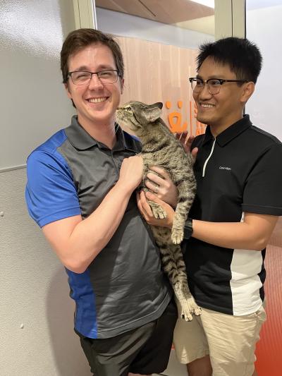 Smiling couple holding Eustace the tabby cat between them