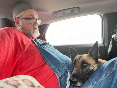 David Herrin sitting in a vehicle with Preciosa the dog's head in his lap