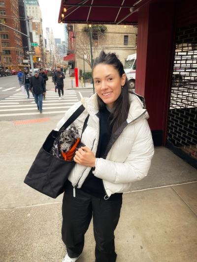 Liana outside holding a black bag with Sonny the puppy's head poking out of the top