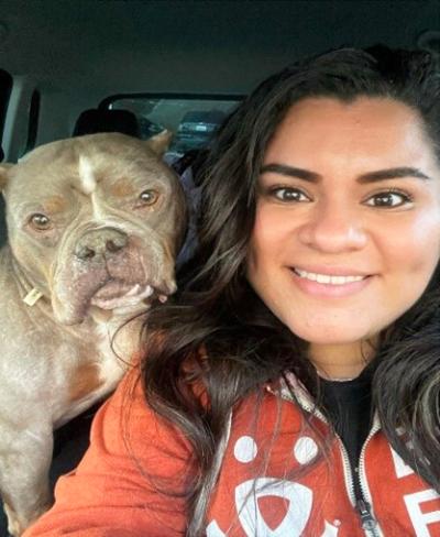 Smiling person wearing a Best Friends zip up sweatshirt next to a dog in a vehicle