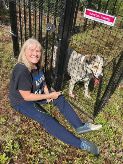 Person sitting next to Barley the dog in a large kennel