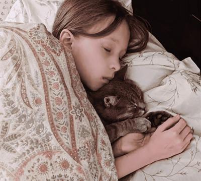 Arsenii sleeping cuddled next to her tabby cat