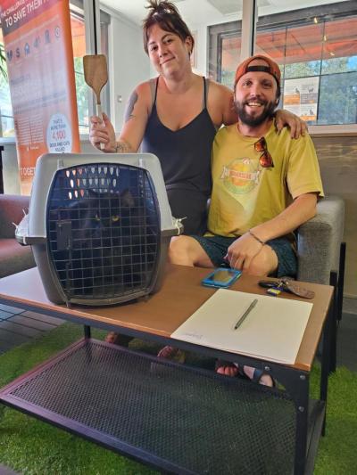 Two people next to Baymax the cat in a kennel and one holding the spatula