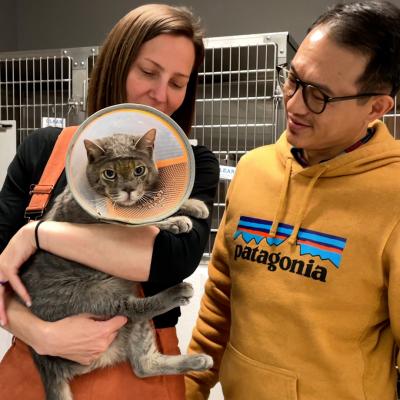 Dr. Christina Boekhout holding Stone Cold the cat with her husband in front of stainless steel kennels