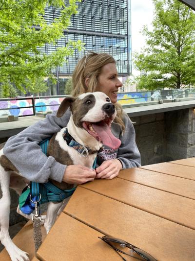 Person hugging Pilsner the dog while sitting at an outside table