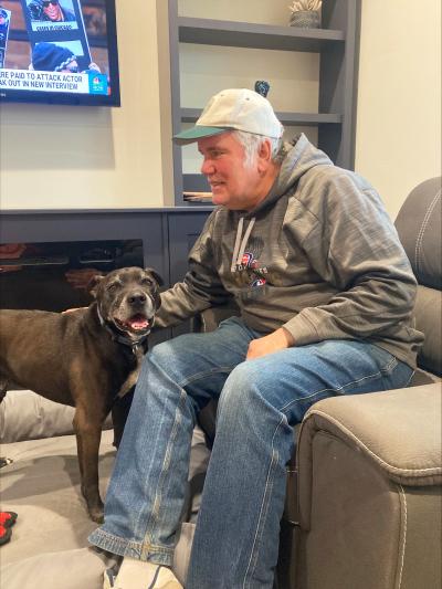 Volunteer Dan Fishbein sitting in a chair petting Chaplin the dog