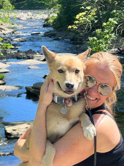 Volunteer Vicki Williams holding Sunny, her dog, in front of a stream