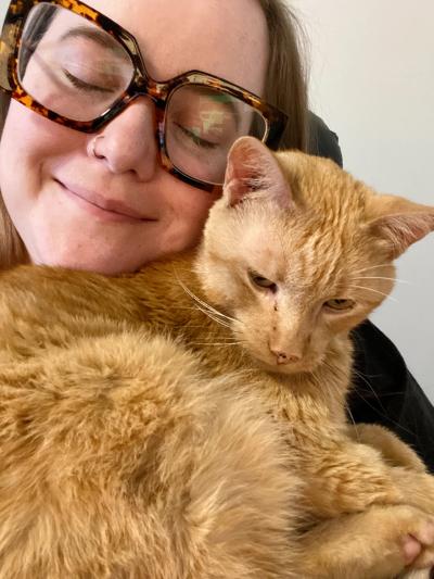 Smiling person with eyes closed and smiling with face next to Wilbur the cat