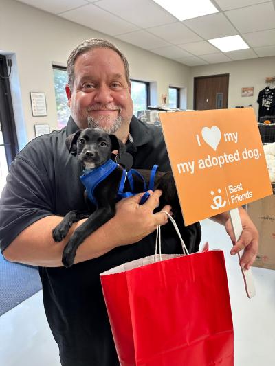 Person holding Iceman the puppy along with a red bag and a sign that says, "I heart my adopted dog"