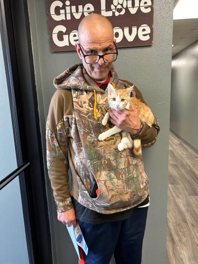 Person holding an orange and white kitten in front of a sign that says Give Love Get Love